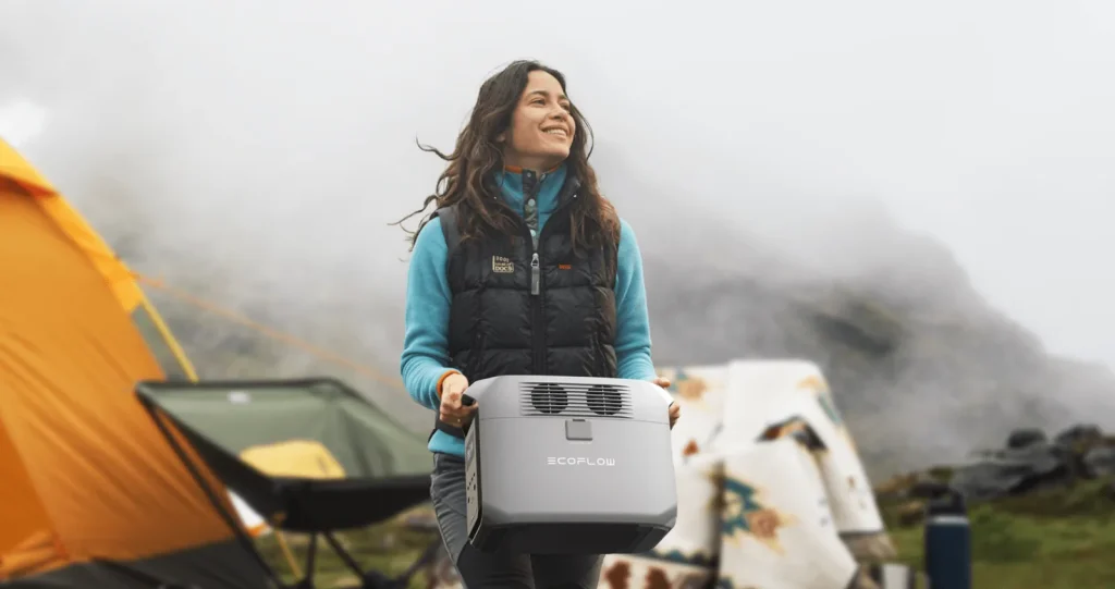 Женщина несет зарядную станцию EcoFlow DELTA 3 1500 возле палатки в горах