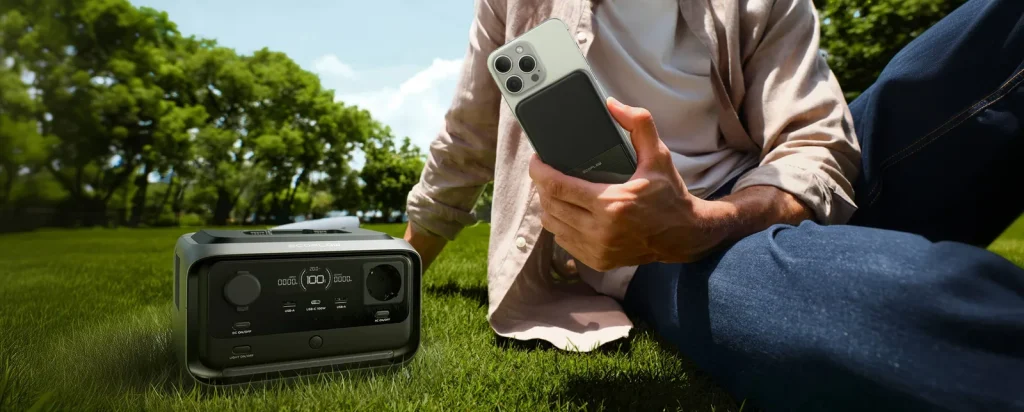 An EcoFlow RIVER 3 Plus Wireless on the grass, its owner holding a phone with a RAPID power bank attached