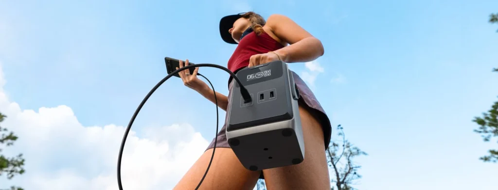 An EcoFlow TRAIL 200 DC in a hand, a smartphone charging from the USB-C port