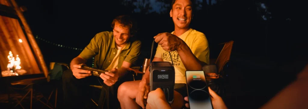 Friends by a campfire holding an EcoFlow TRAIL 200 DC that charges a phone and a console