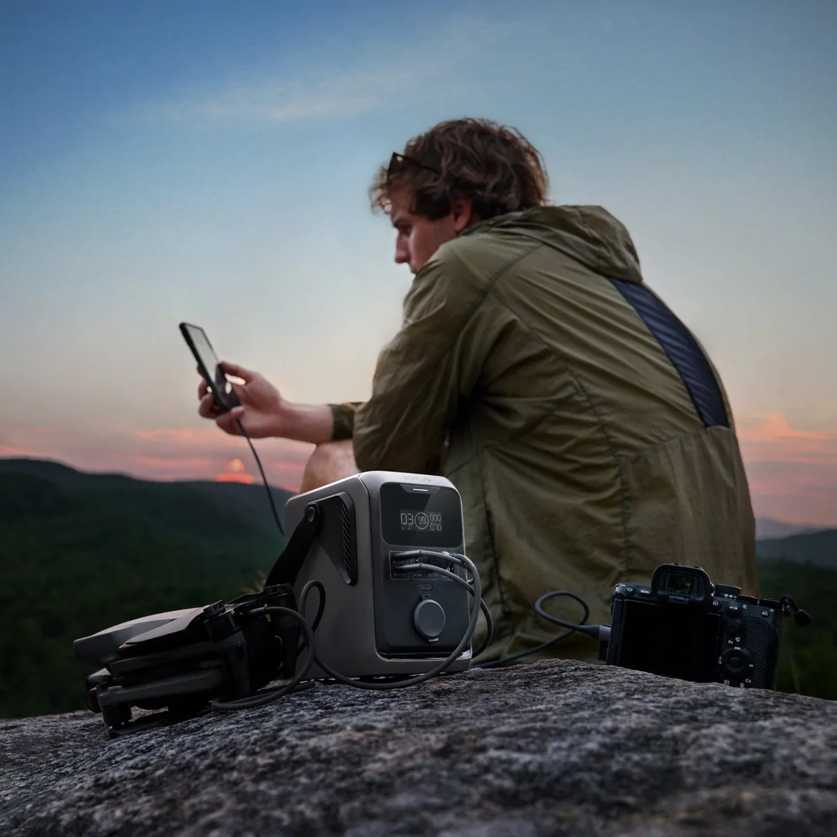Турист на скелі на заході сонця заряджає телефон від EcoFlow TRAIL 300 DC